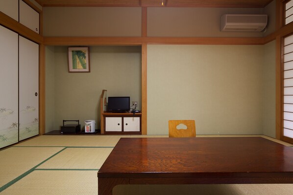 Una habitación tradicional japonesa con suelo de tatami, una mesa de madera, un televisor sobre un mueble bajo y puertas correderas.