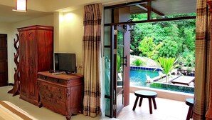 Una habitación con un armario de madera, televisión y vistas a una piscina y follaje.