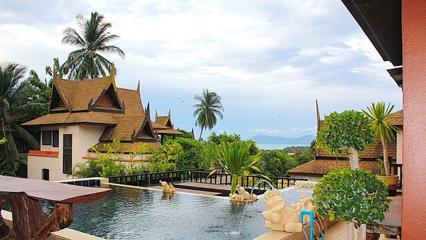Una piscina con cubierta de madera, rodeada de plantas tropicales y arquitectura tradicional.