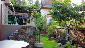 Un muro de piedra, una pérgola de madera y una pequeña cascada en un jardín.