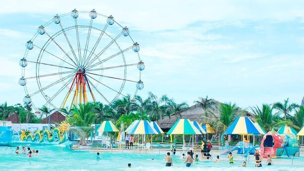 Une plage avec une grande roue, des palmiers et des parasols colorés.