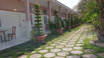A hotel corridor with hexagonal stone flooring, potted topiary trees, and a row of chairs along the left side.