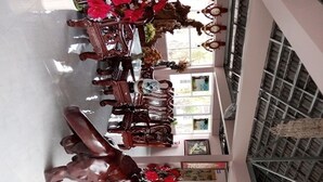 Un vaste atrium doté d’un haut plafond, avec un espace de détente central comprenant une table et des chaises en bois, le tout agrémenté de fleurs rouges et d’éléments décoratifs.