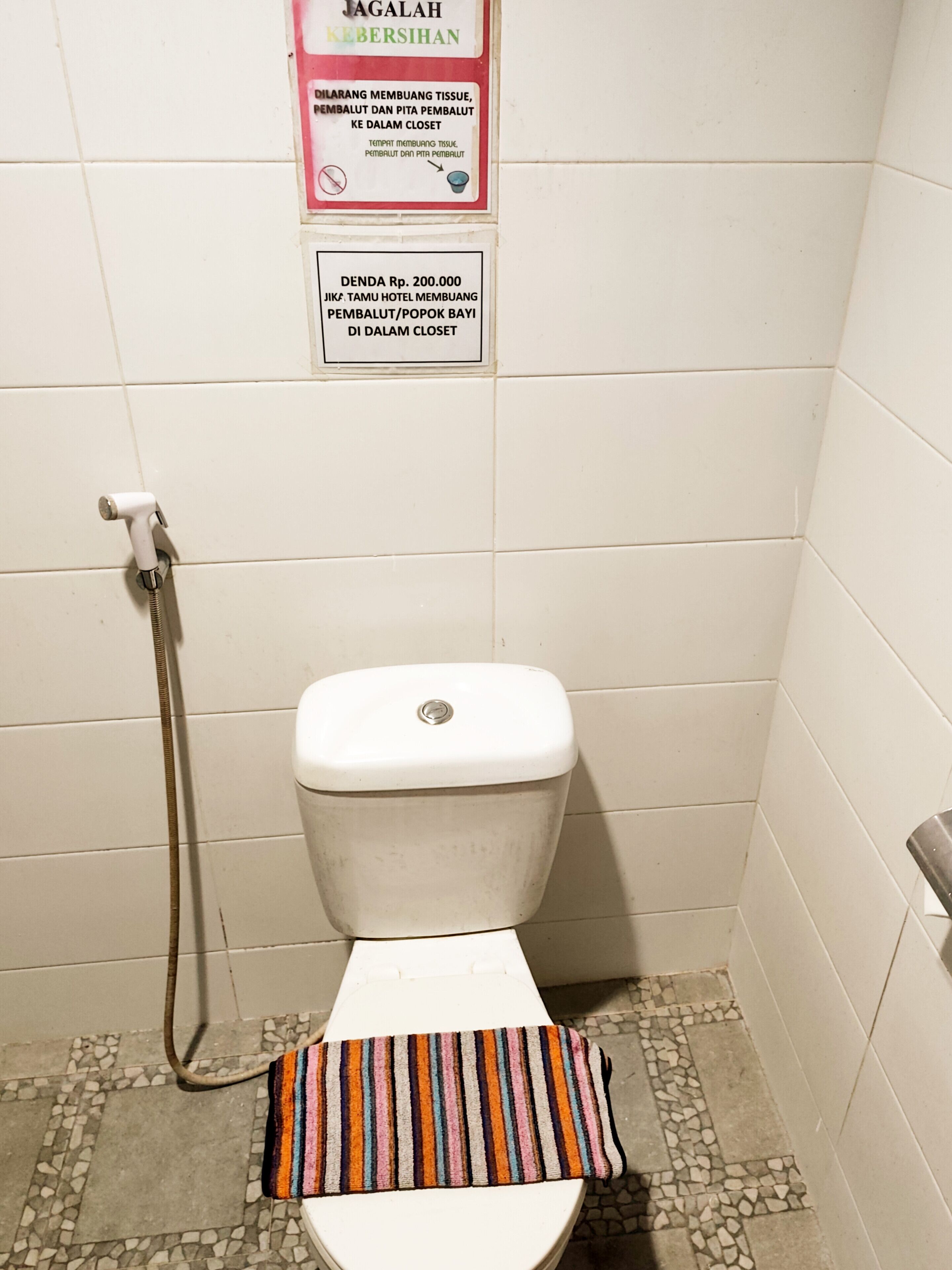 Un baño pequeño con azulejos, un inodoro, una ducha y un tapete a rayas en el suelo.