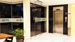 A hotel entrance with a reception desk, a potted plant, and an elevator. - Grace Setia Hotel (Surabaya)