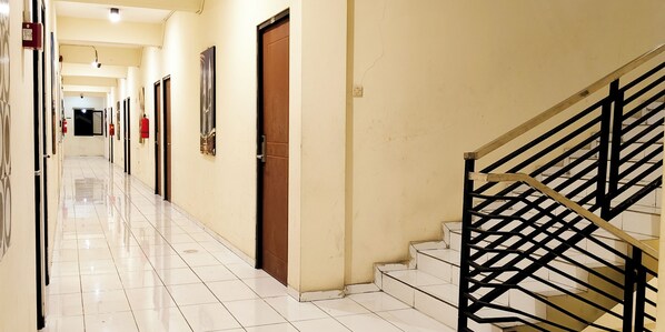 Un pasillo de hotel con suelo de baldosas, puertas y una escalera con barandilla metálica.