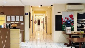 A hotel reception area with a reception desk, a coffee machine, and a dining area with a table and chairs. - Grace Setia Hotel (Surabaya)