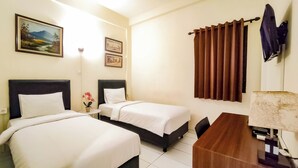 A hotel room with two beds, a desk, a lamp, and a painting on the wall. - Grace Setia Hotel (Surabaya)