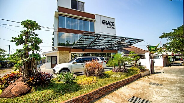 A modern hotel with a glass canopy entrance, a white car parked in front, and landscaped garden beds. - Grace Setia Hotel (Surabaya)