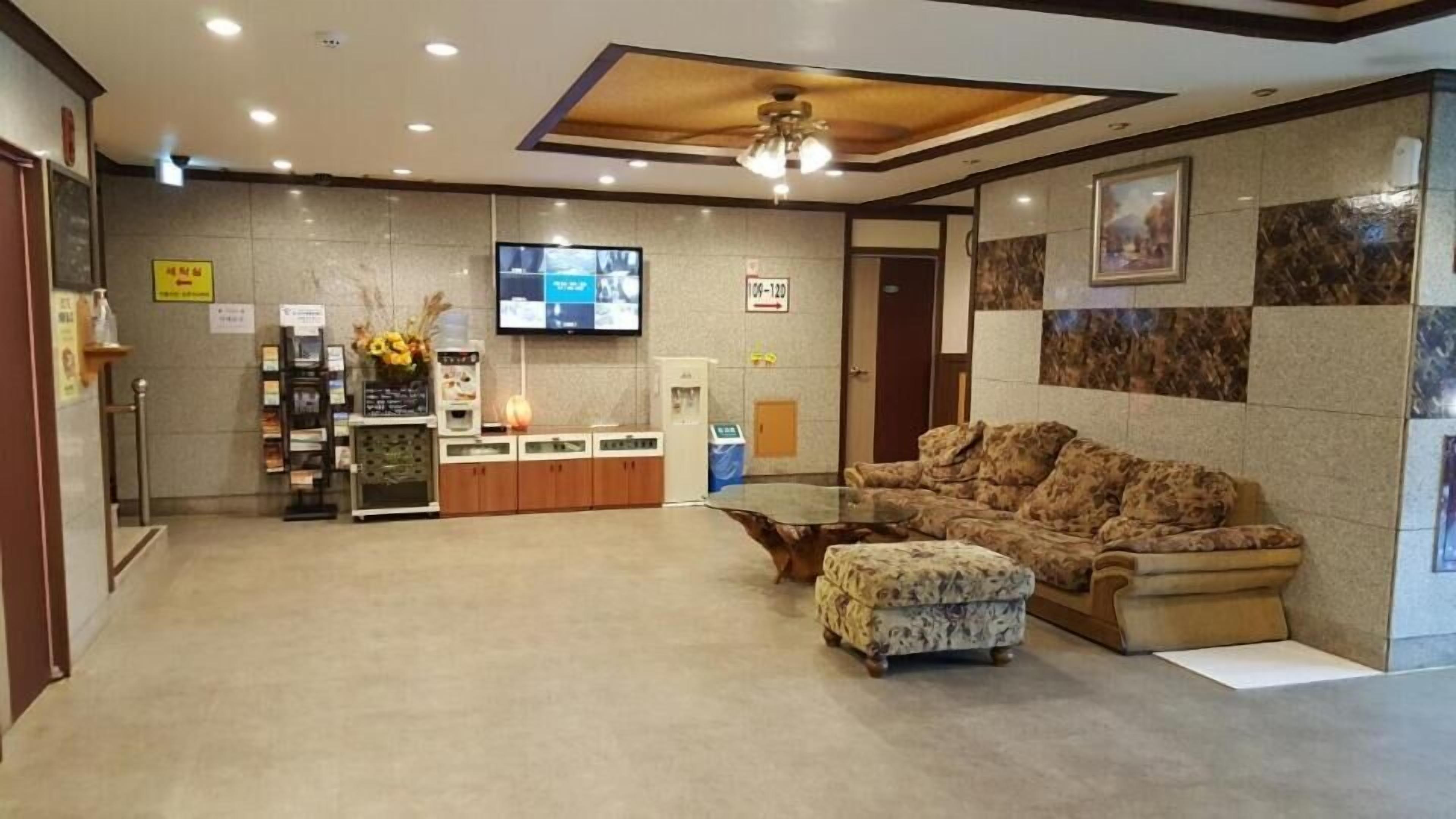 A lobby with a reception desk, a flat-screen TV, a sofa, and a coffee machine.