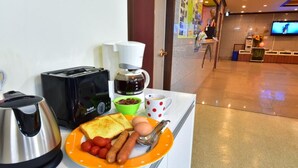 Montaje de desayuno de hotel con tostadora, cafetera, hervidor y un plato con tostadas, huevos y salchichas.