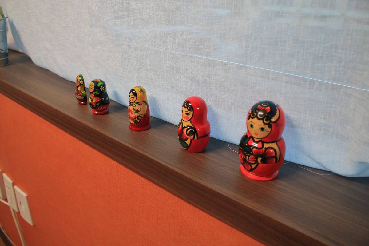 A row of traditional Russian Matryoshka dolls on a wooden shelf against a white wall.