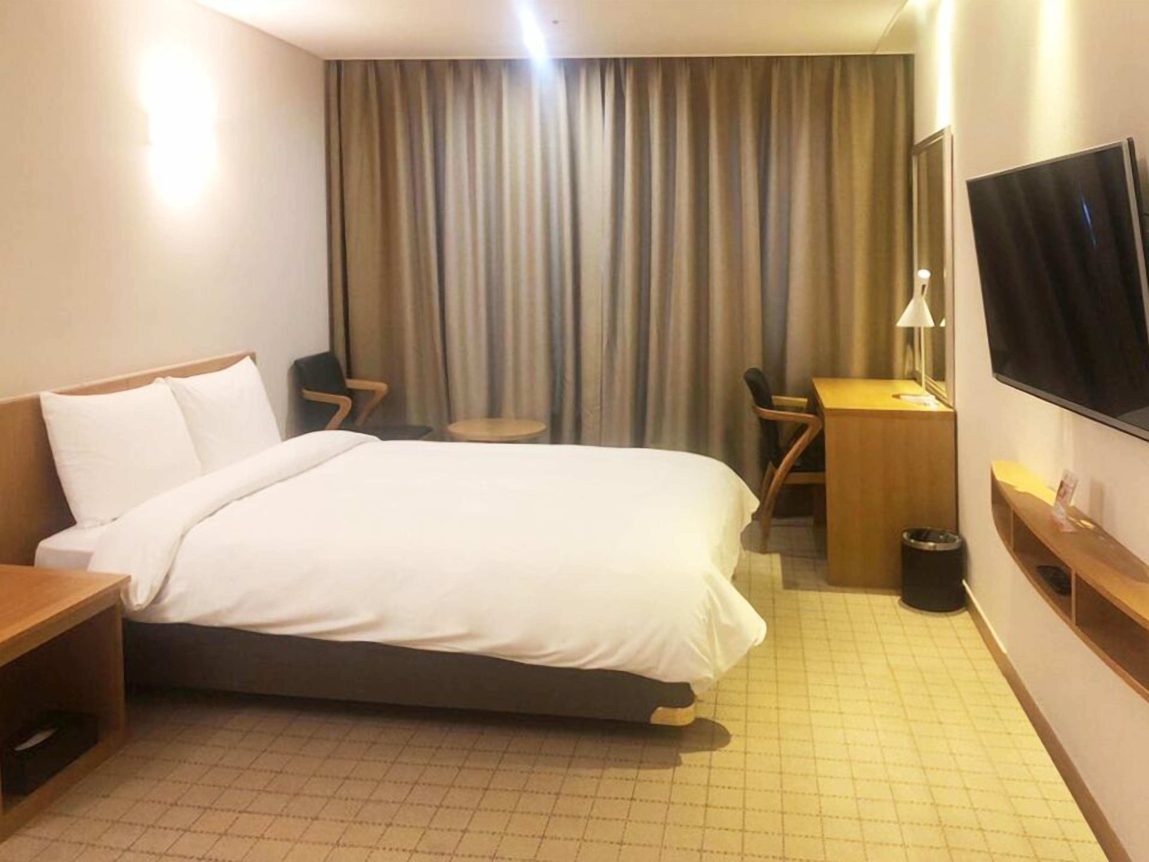 A hotel room with a bed, a desk, a chair, a TV, and a window with curtains.