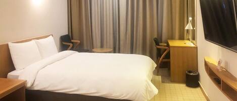 A hotel room with a bed, a desk, a chair, a TV, and a window with curtains.