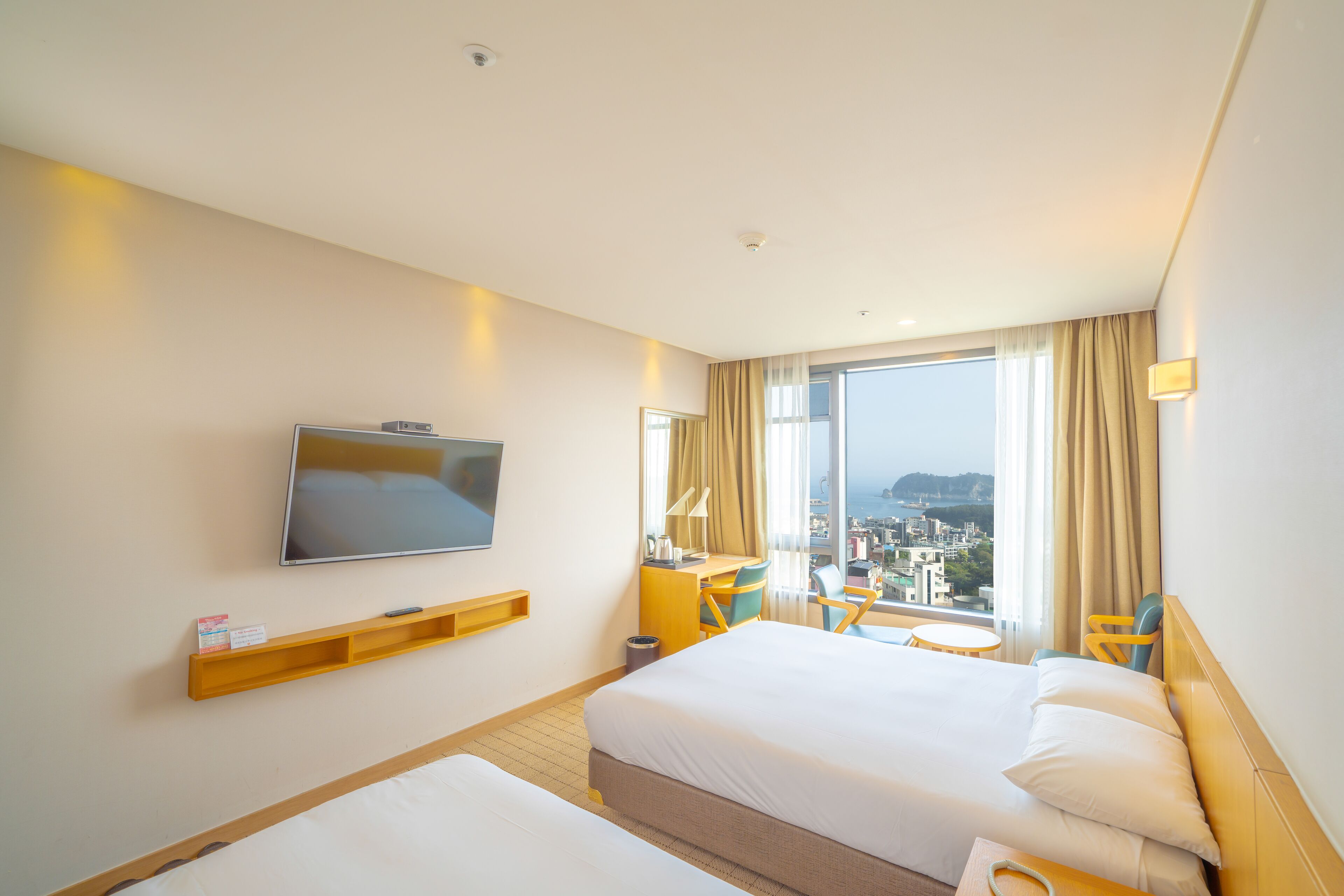 A hotel room with two beds, a TV, a desk, a chair, and a view of the city.