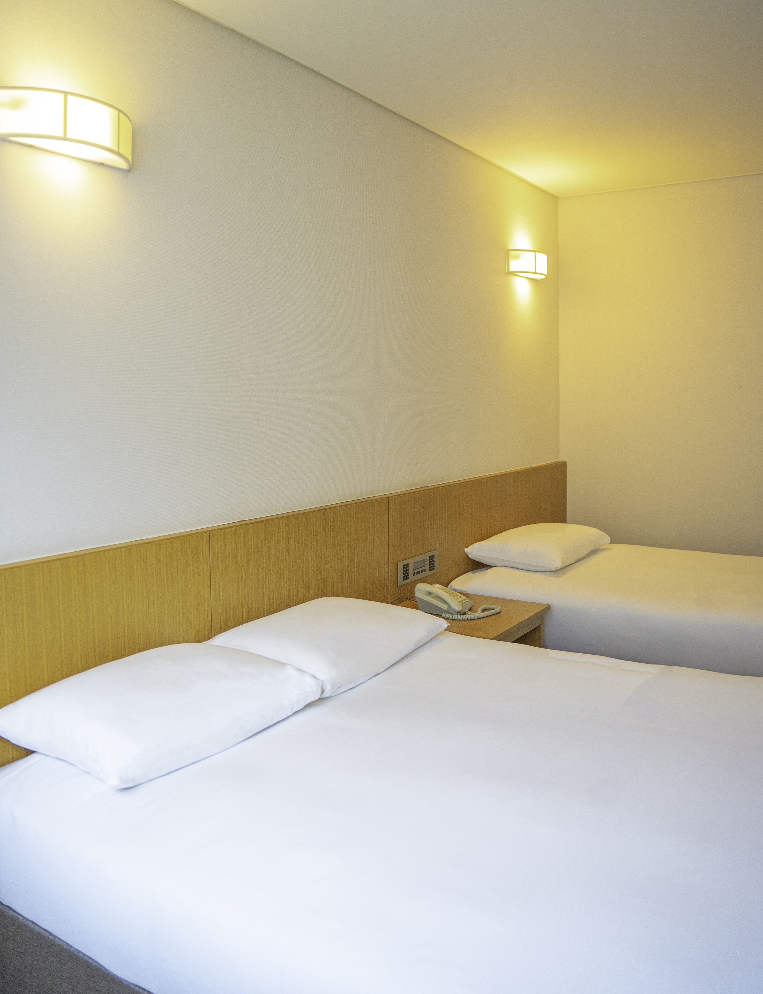 Habitación de hotel con dos camas, teléfono en la mesita de noche e iluminación en la pared.