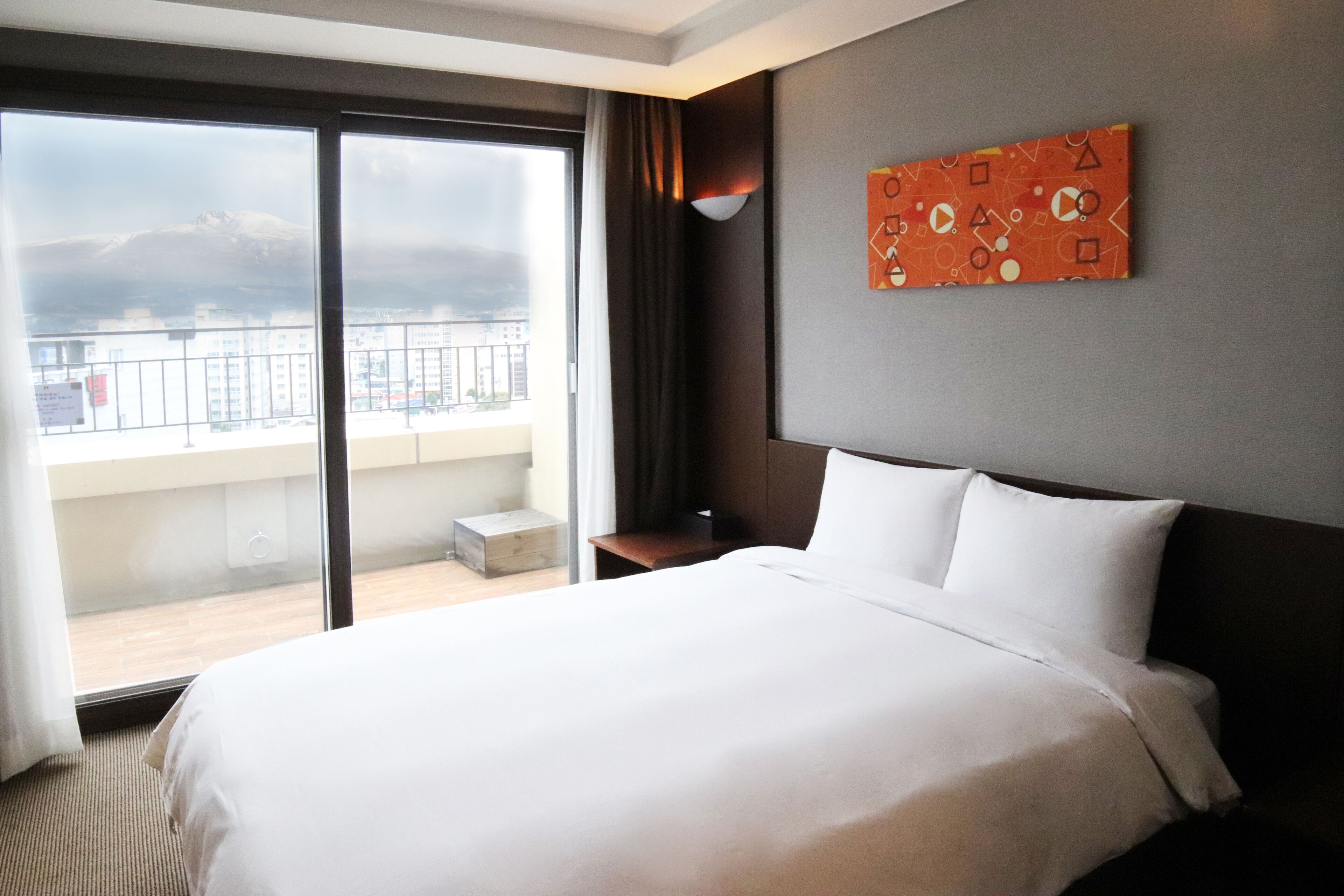 Habitación de hotel con una cama grande, vista de la ciudad desde un balcón y una obra de arte colgada en la pared.