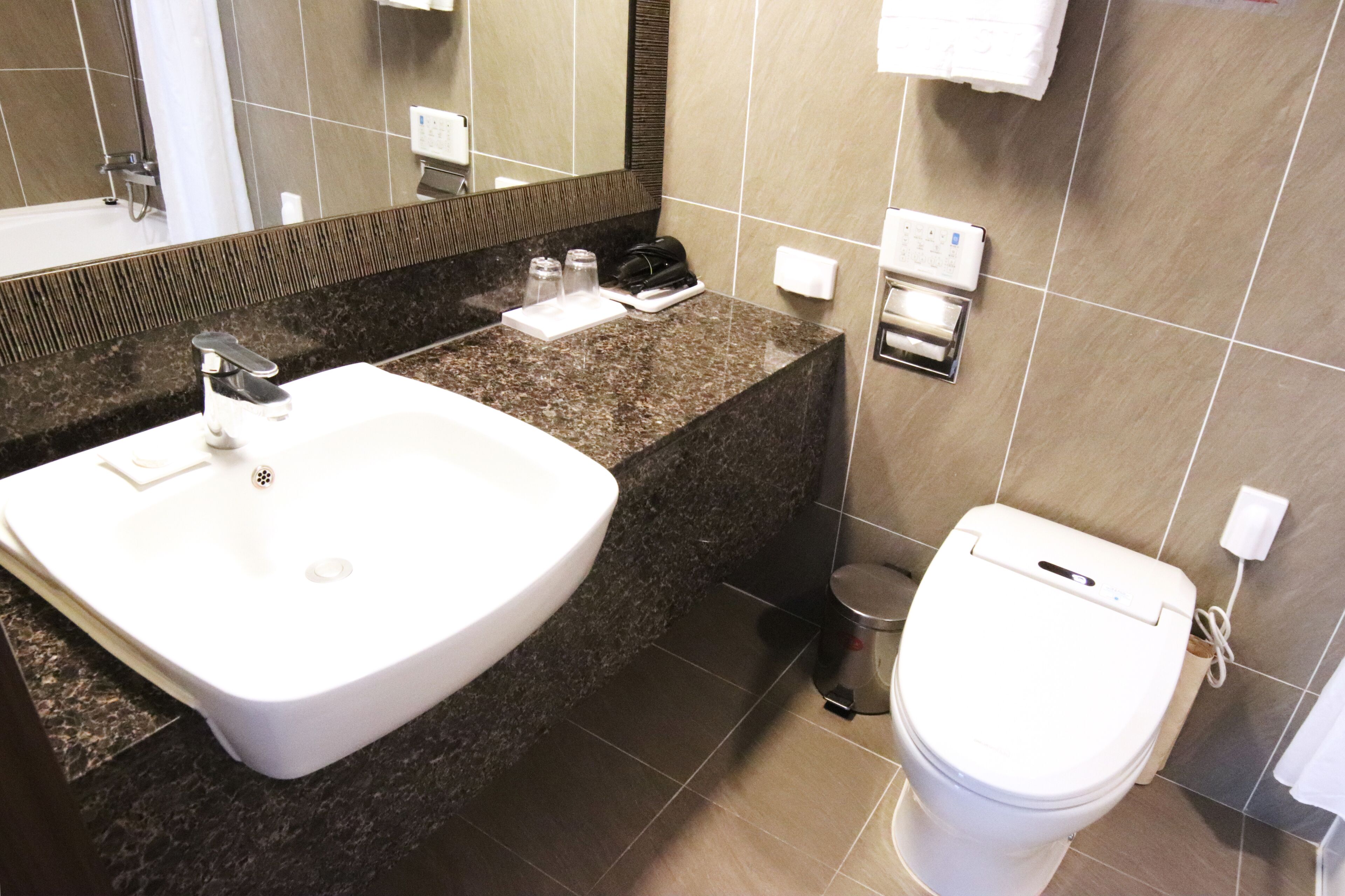 A modern bathroom with a white sink, dark granite countertop, a mirror, a toilet, and a trash can.