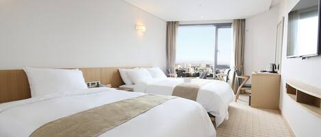 A hotel room with two beds, a desk, a chair, a TV, and a large window with a city view.