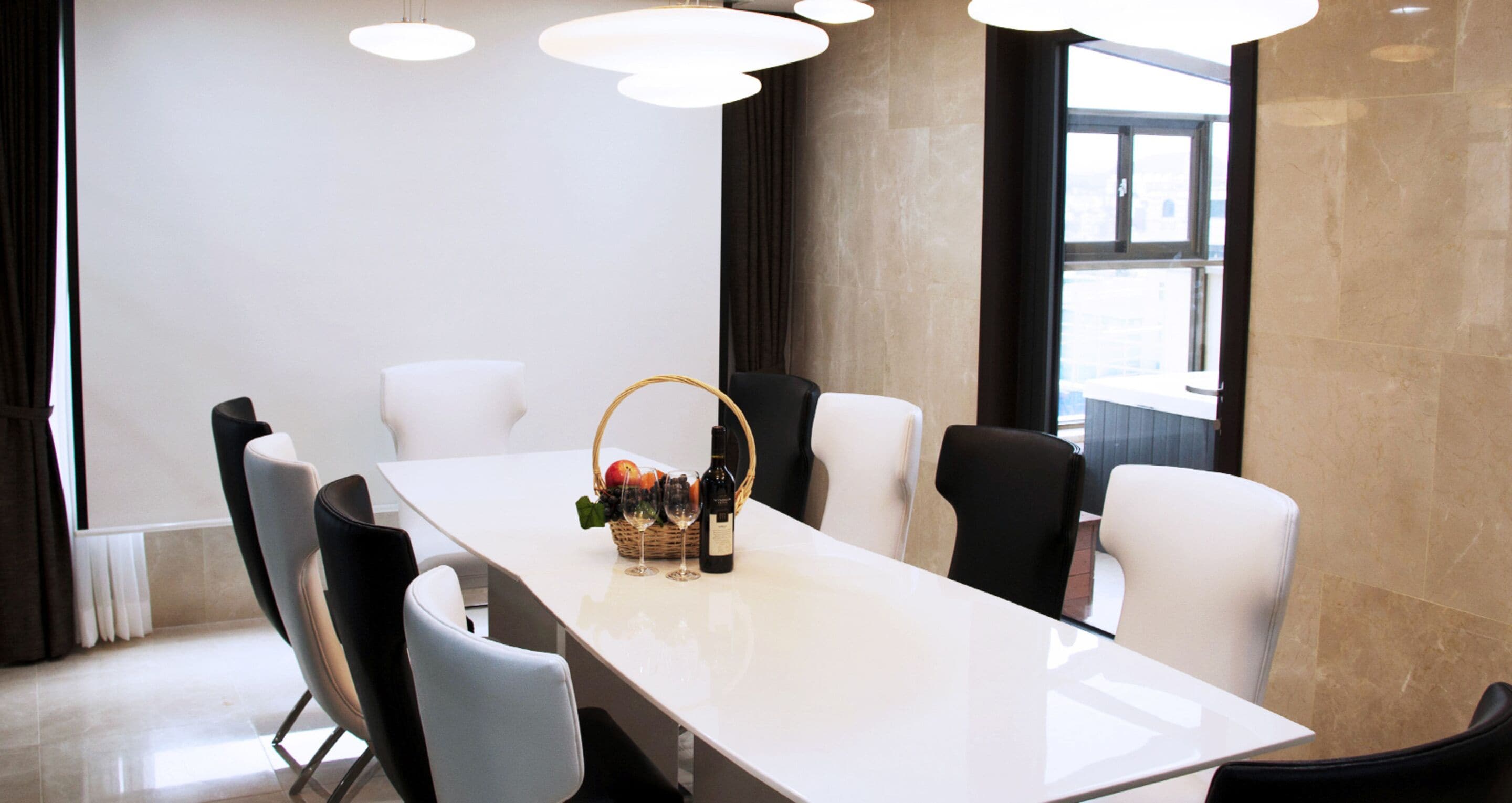 Un espace repas moderne avec une longue table, des chaises blanches et un panier rempli de fruits, ainsi que des verres à vin.