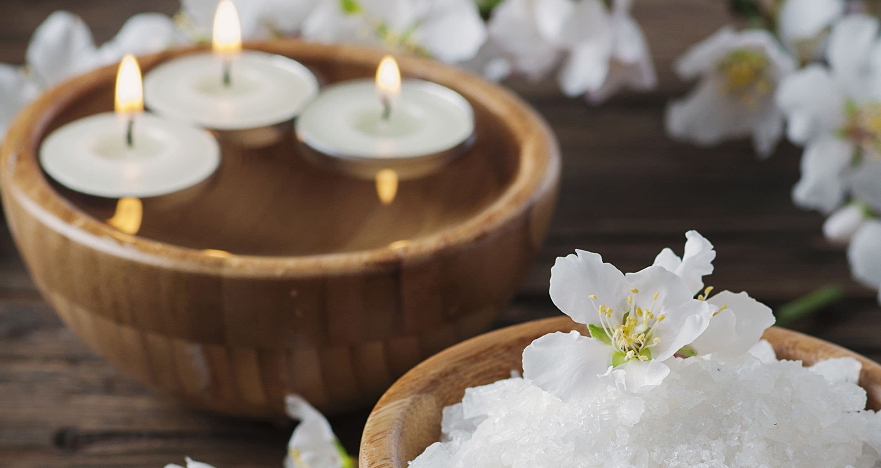 A wooden bowl with four lit candles and white flowers.