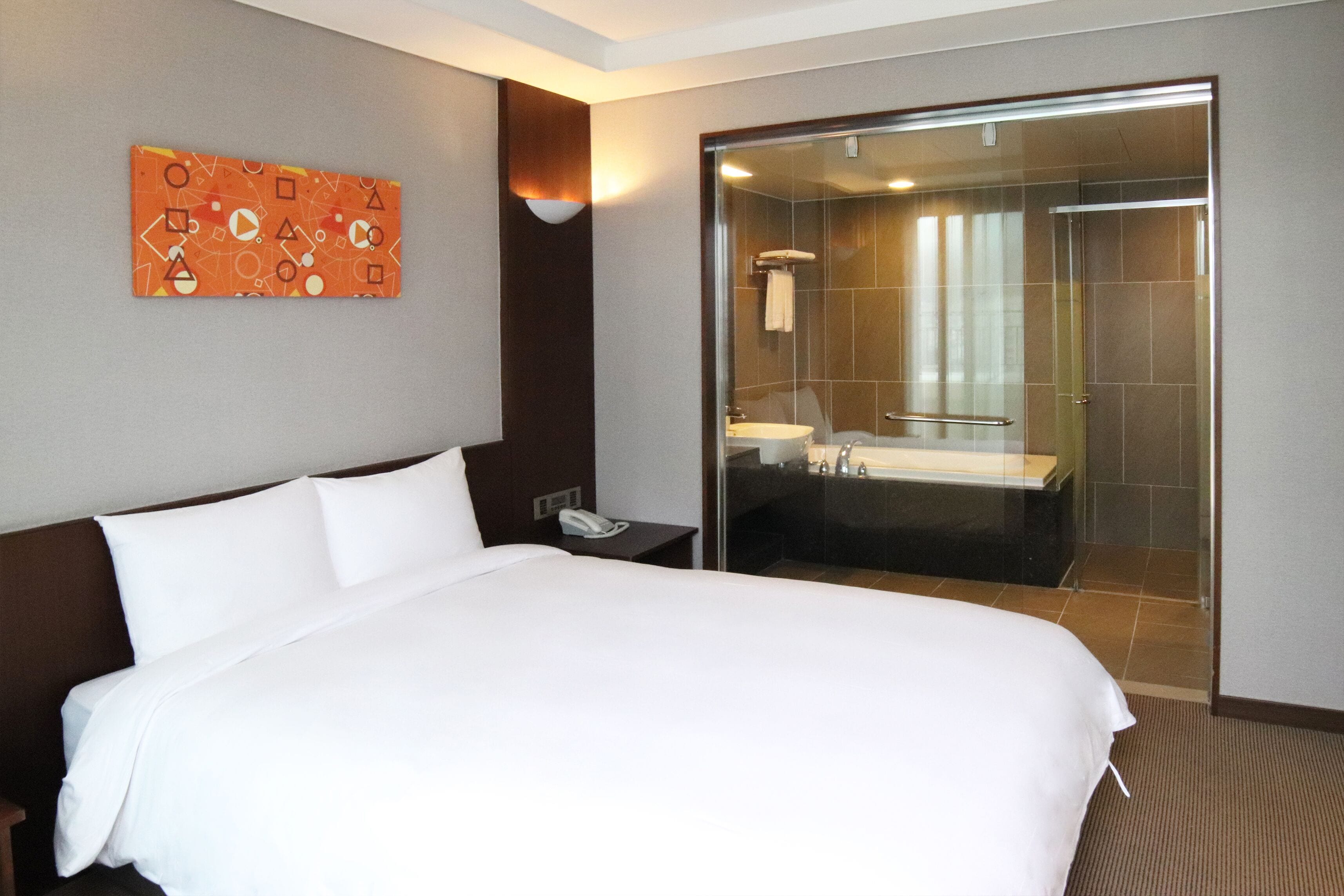 A hotel room with a large bed, a bedside phone, a glass-enclosed shower, and a bathroom with a sink and mirror.