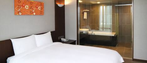 A hotel room with a large bed, a bedside phone, a glass-enclosed shower, and a bathroom with a sink and mirror.