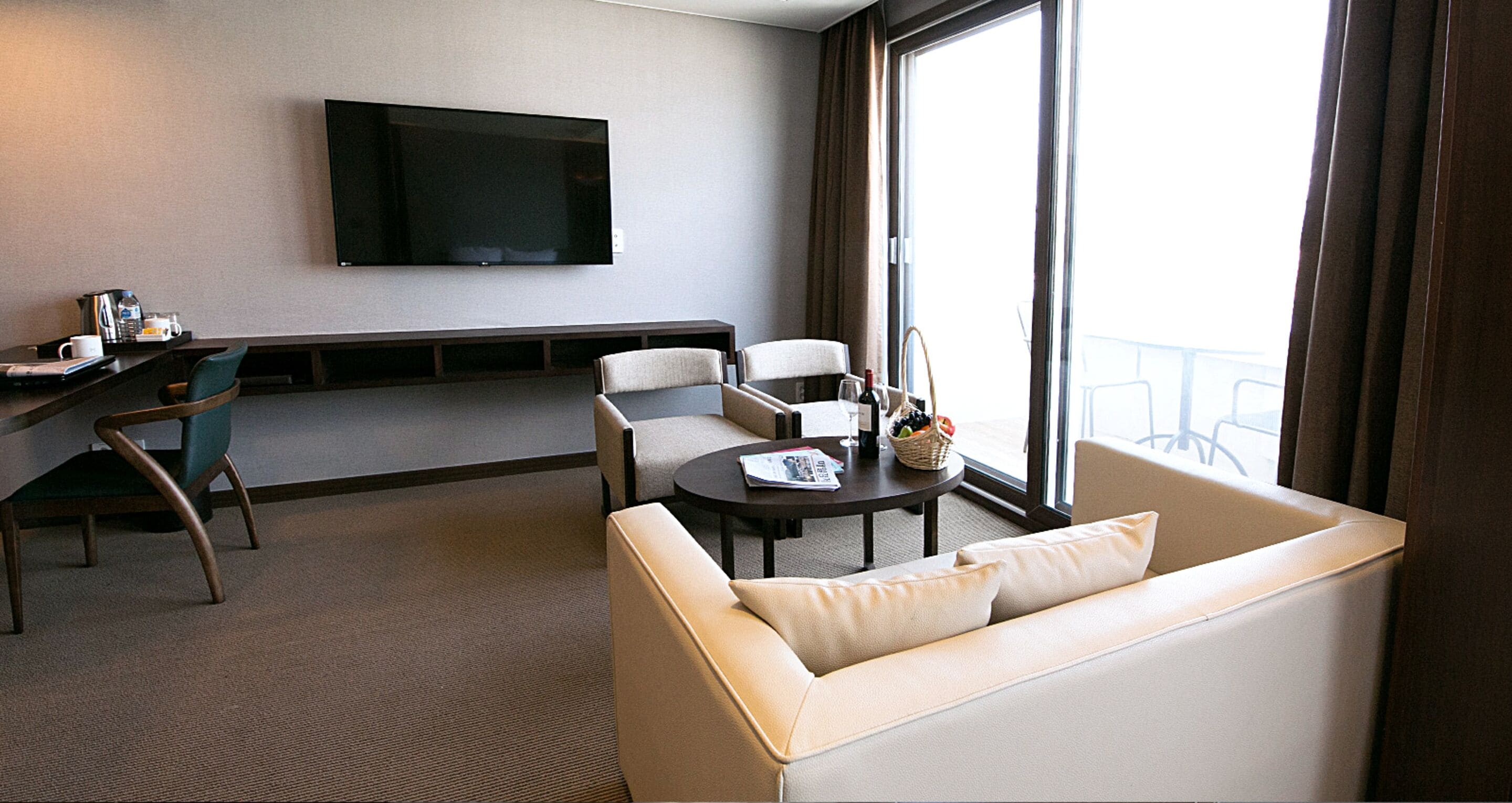 Habitación de hotel con sofá, sillas, una mesita, televisor de pantalla plana y ventana grande.