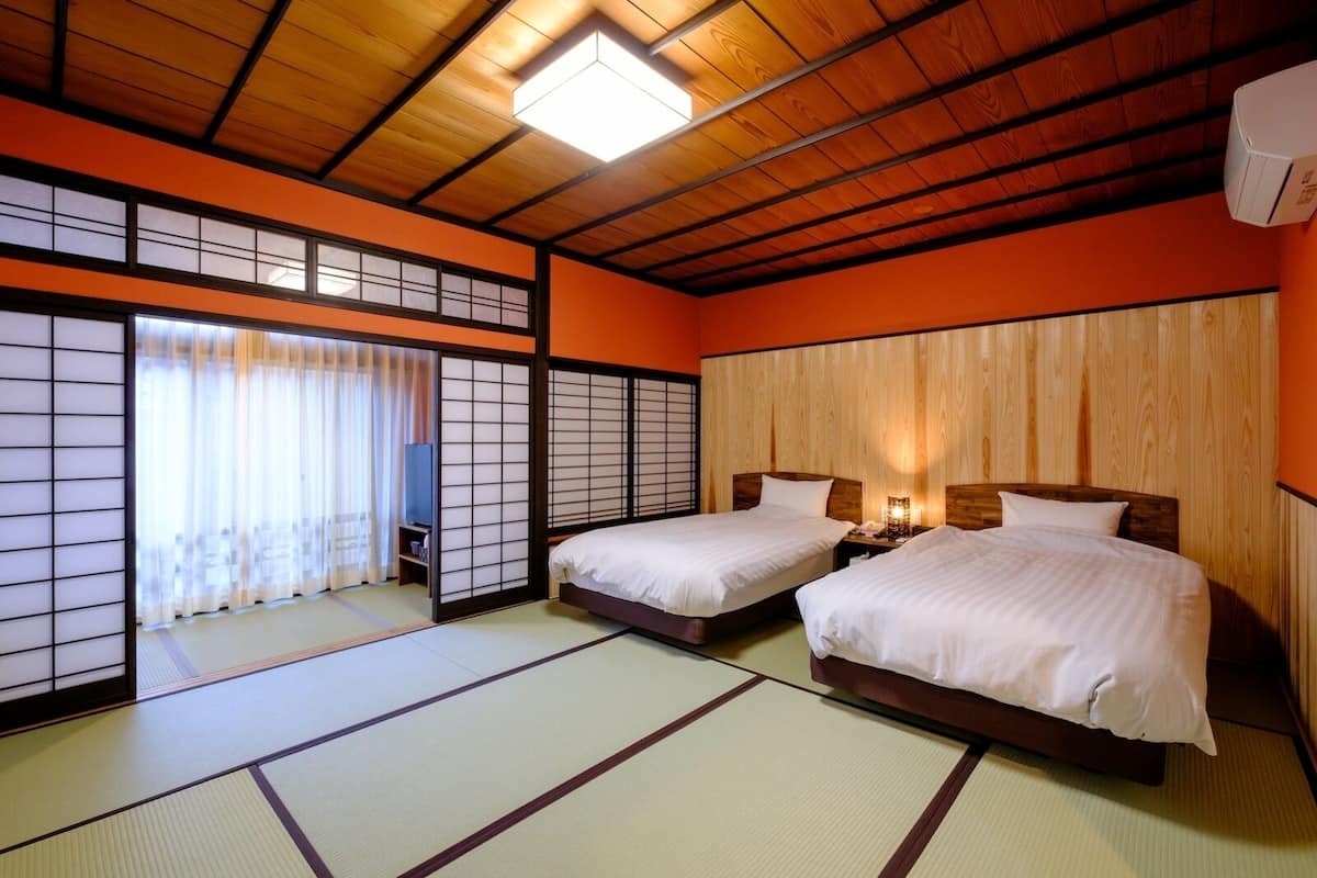 A traditional Japanese-style room with tatami flooring, two beds, a sliding shoji screen, and a ceiling fan.