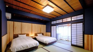 A traditional Japanese-style room with tatami flooring, two single beds, a wooden ceiling, and sliding shoji doors. - Iwayu Ryokan (Misasa)