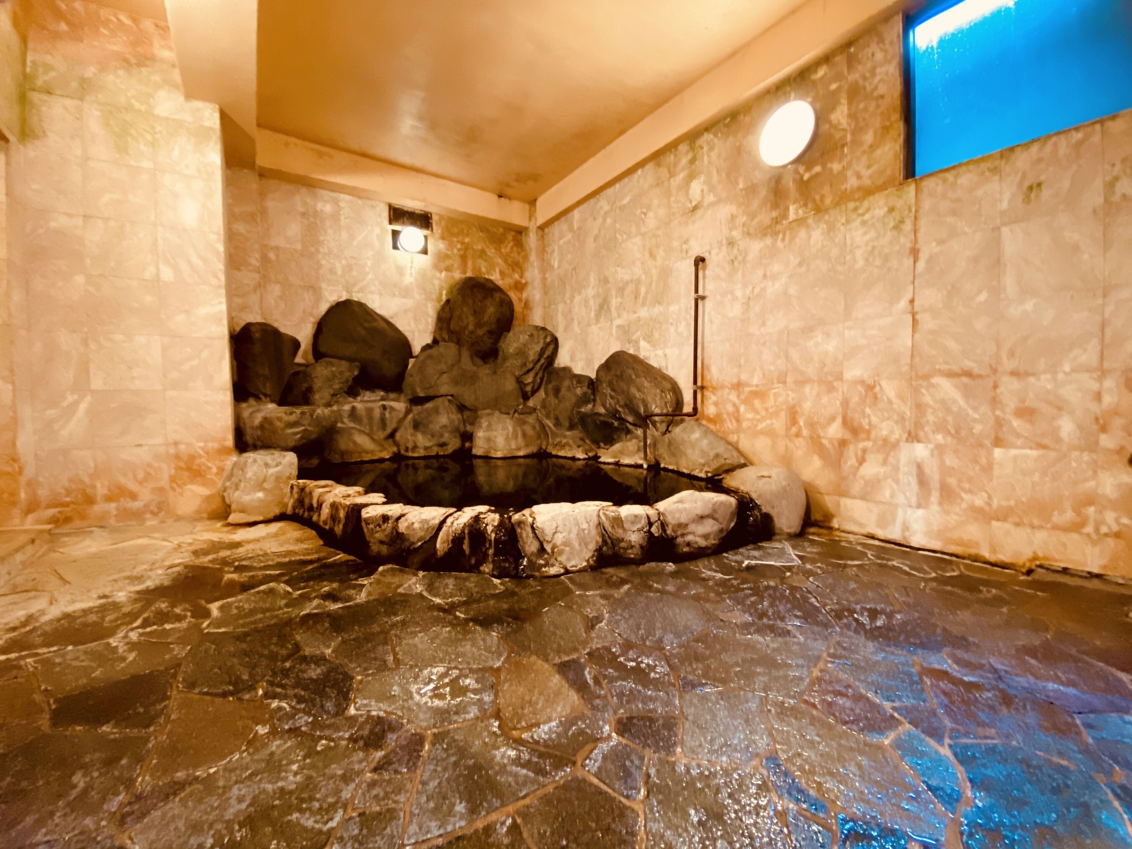 Una bañera de piedra con piso y paredes de piedra, rodeada de rocas.