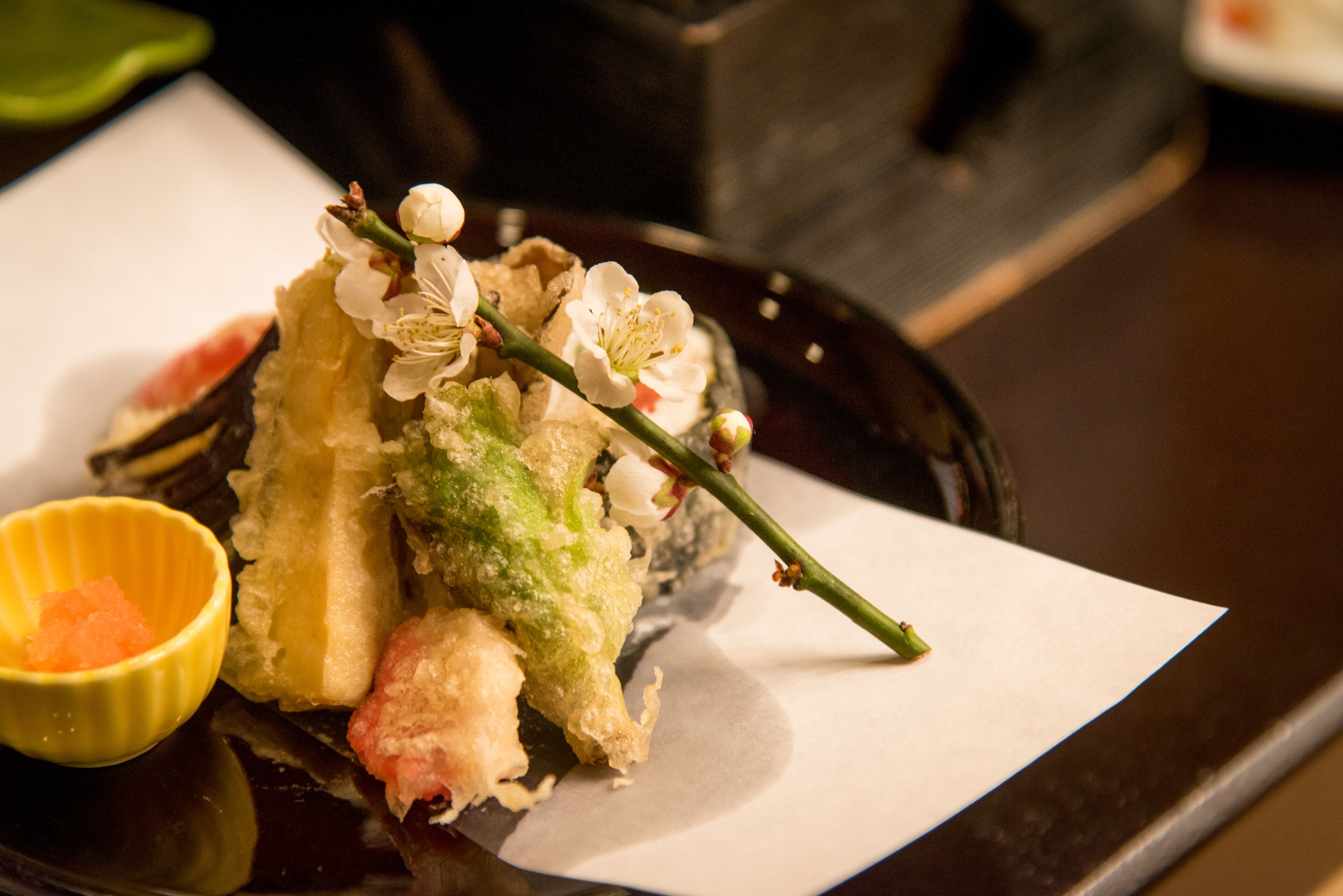 A plate of tempura with a decorative flower and a small bowl of sauce.