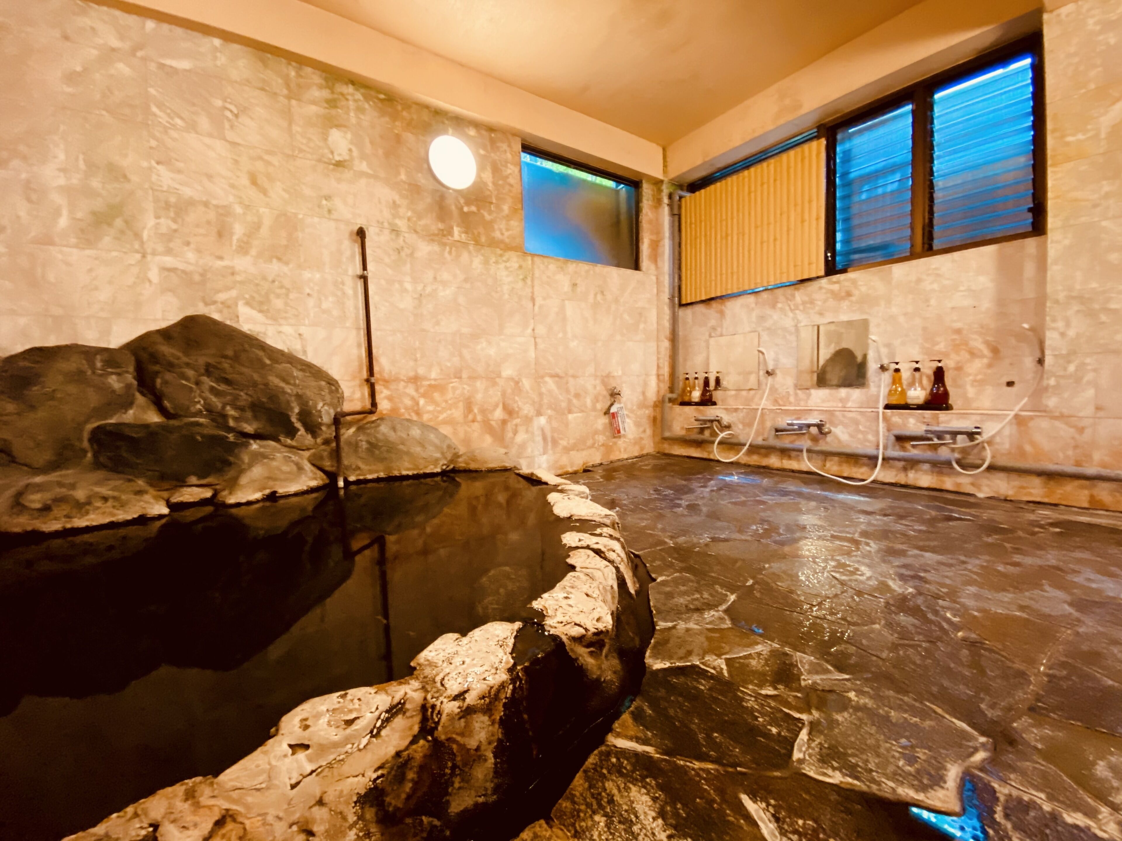 A stone-floored spa area with a hot spring, a stone wall, and a window with blinds.