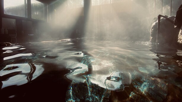 A hot spring area with clear water, rocks, and sunlight streaming through windows. - Iwayu Ryokan (Misasa)