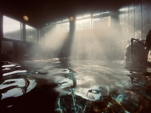 A hot spring area with clear water, rocks, and sunlight streaming through windows. - Iwayu Ryokan (Misasa)