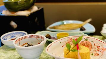 A table set with various dishes, including a bowl with a yellow item and green leaves, and a green teapot in the background.