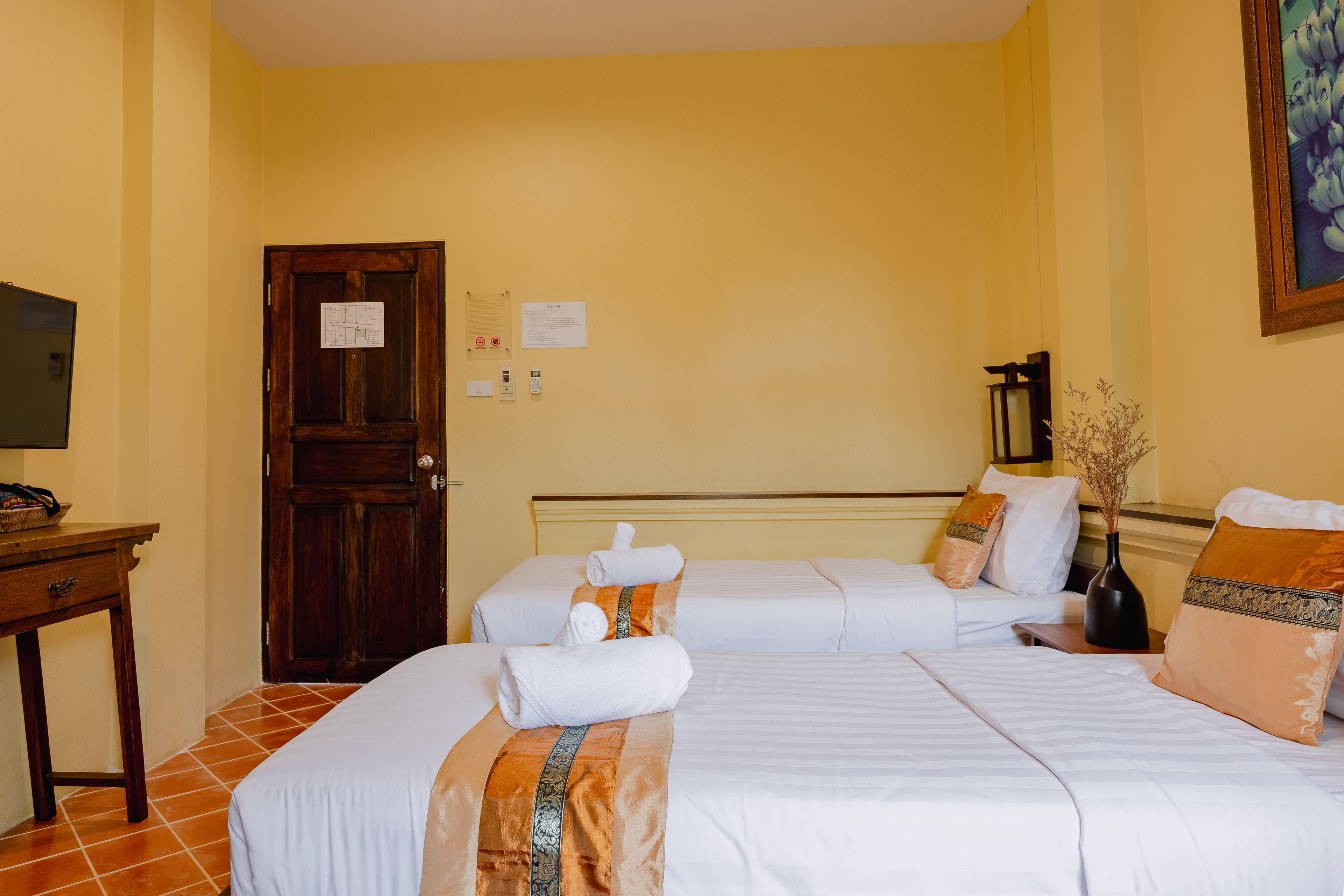 Une chambre d’hôtel avec deux lits, une porte en bois, un bureau et un tableau au mur.