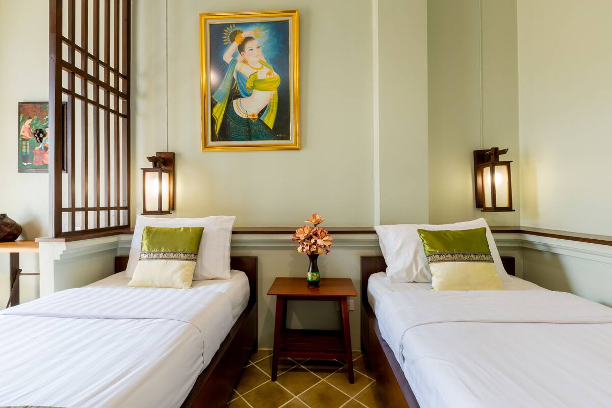 A hotel room with two beds, a nightstand with a vase of flowers, and wall-mounted lamps.
