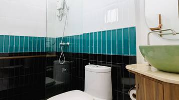Ein modernes Badezimmer mit Toilette in Weiß, einem grünen Waschbecken und einer Duschkabine aus Glas.