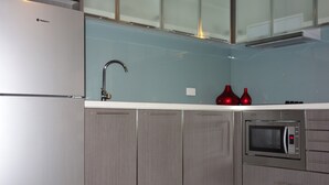 A kitchen with a stainless steel refrigerator, a microwave, and a sink with a modern faucet. - Glenelg Gateway Apartments (Glenelg)