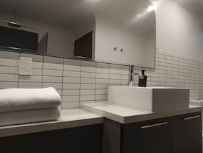 A modern bathroom with a white sink, dark cabinets, and a towel on the counter. - Glenelg Gateway Apartments (Glenelg)