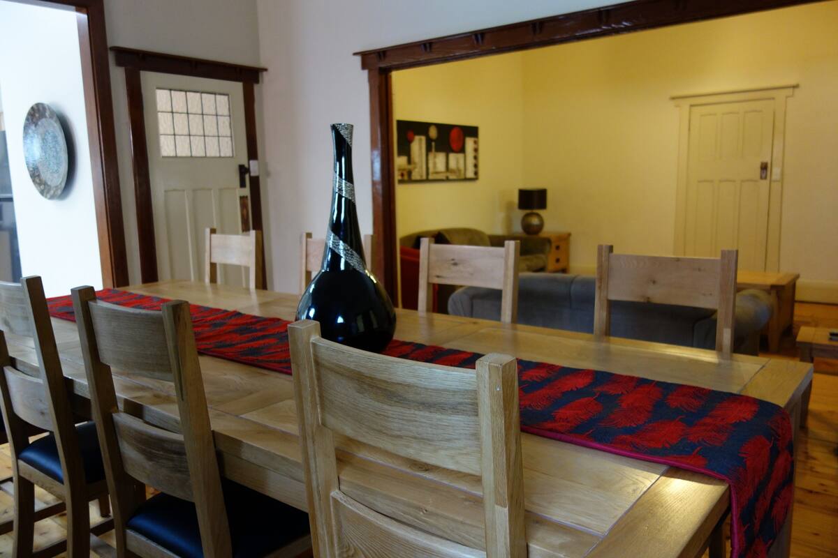 A dining area with a wooden table, chairs, and a vase. There is a door and a window in the background.