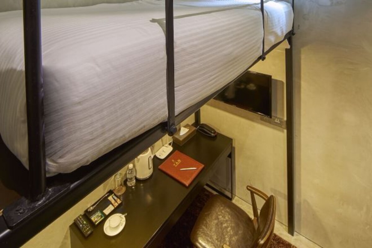 A bunk bed with a mattress, a small table with a notebook, a water bottle, a glass, and a cup.
