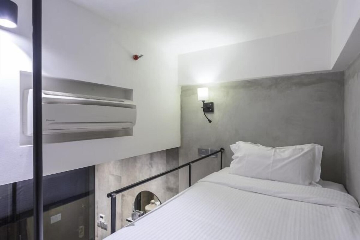 Ein modernes Hotelzimmer mit Bett, Wandklimaanlage, kleinem Fenster und einer Leuchte.