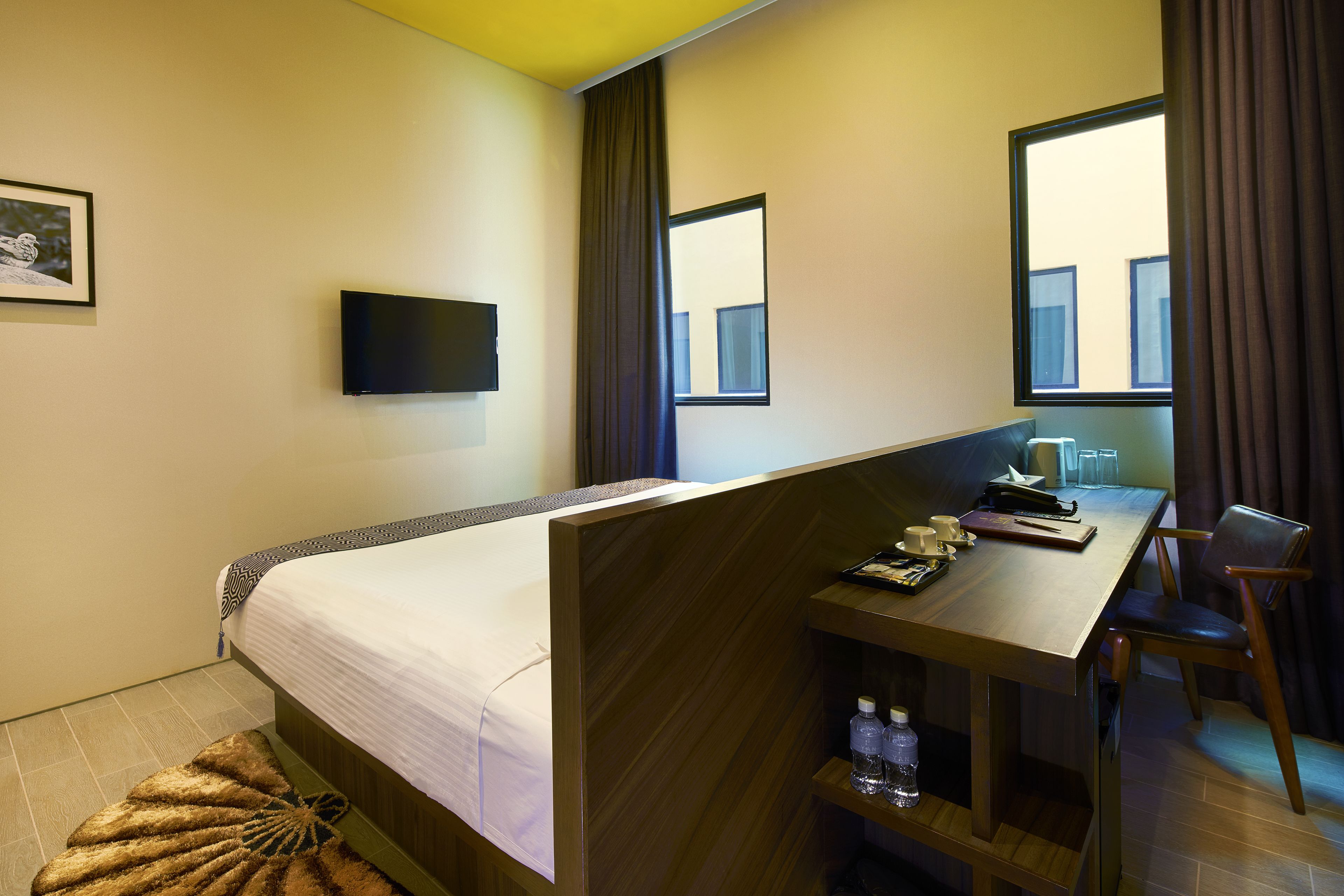 Una habitació d'hotel amb un llit, un escriptori amb una cadira, una televisió i una finestra amb cortines.