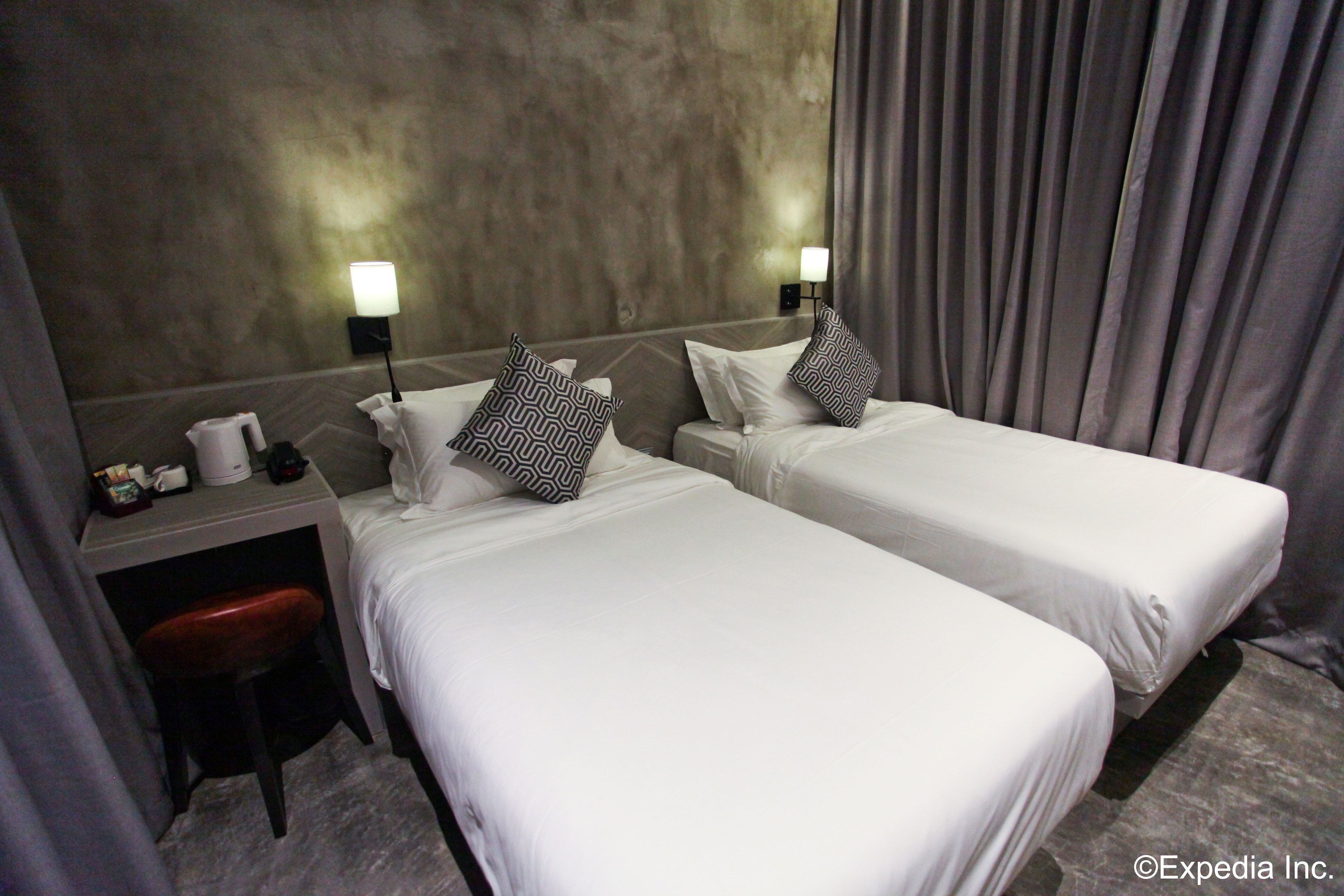 A hotel room with two single beds, a desk with a chair, a lamp, and a nightstand with a coffee maker.
