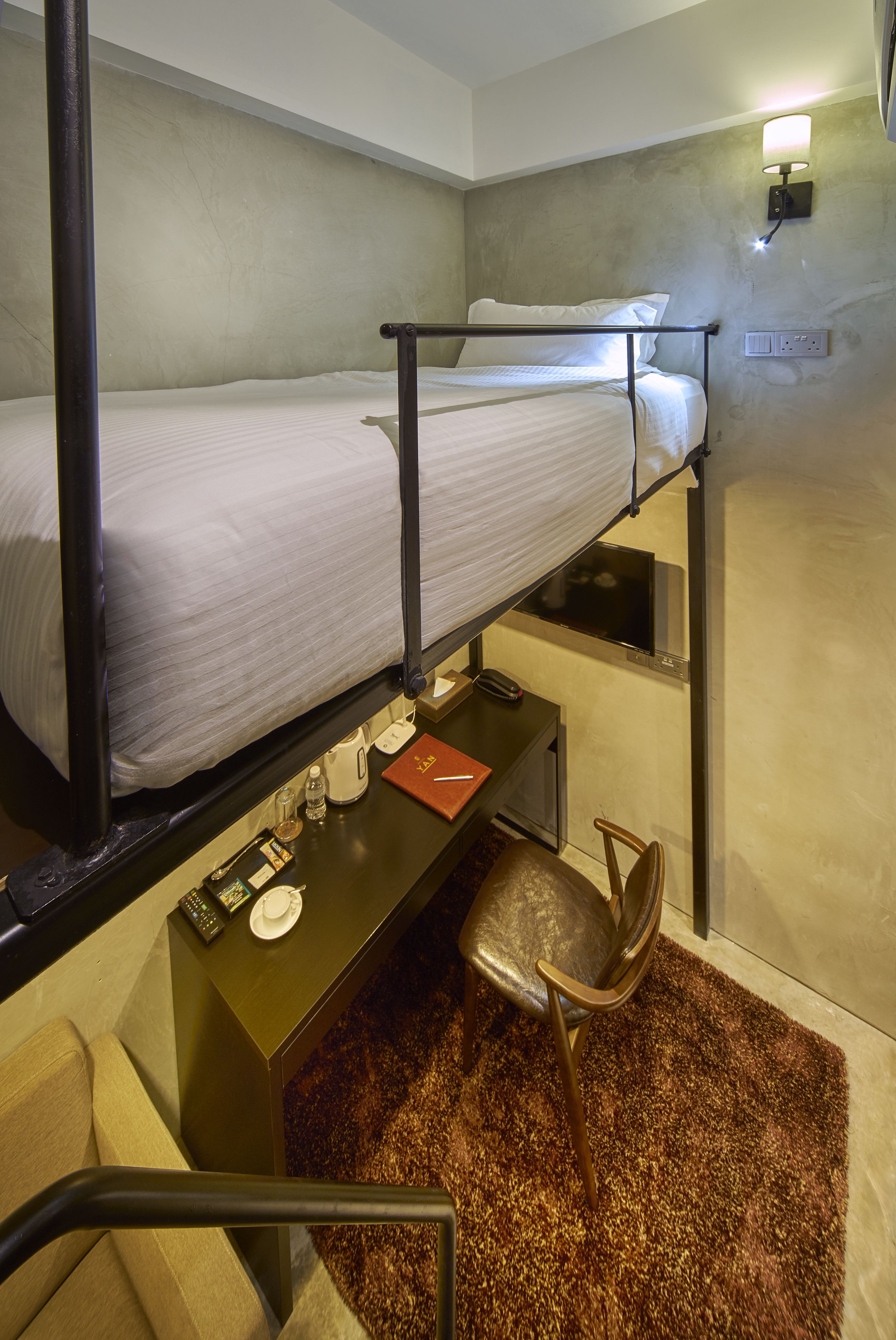 Una cama individual superpuesta con escritorio, silla, televisión y enchufe.