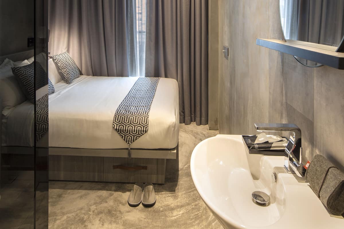 Moderni hotellihuone, jossa on suuri sänky, lasinen suihkuseinä, sisäänrakennettu pesuallas ja suuri peili.