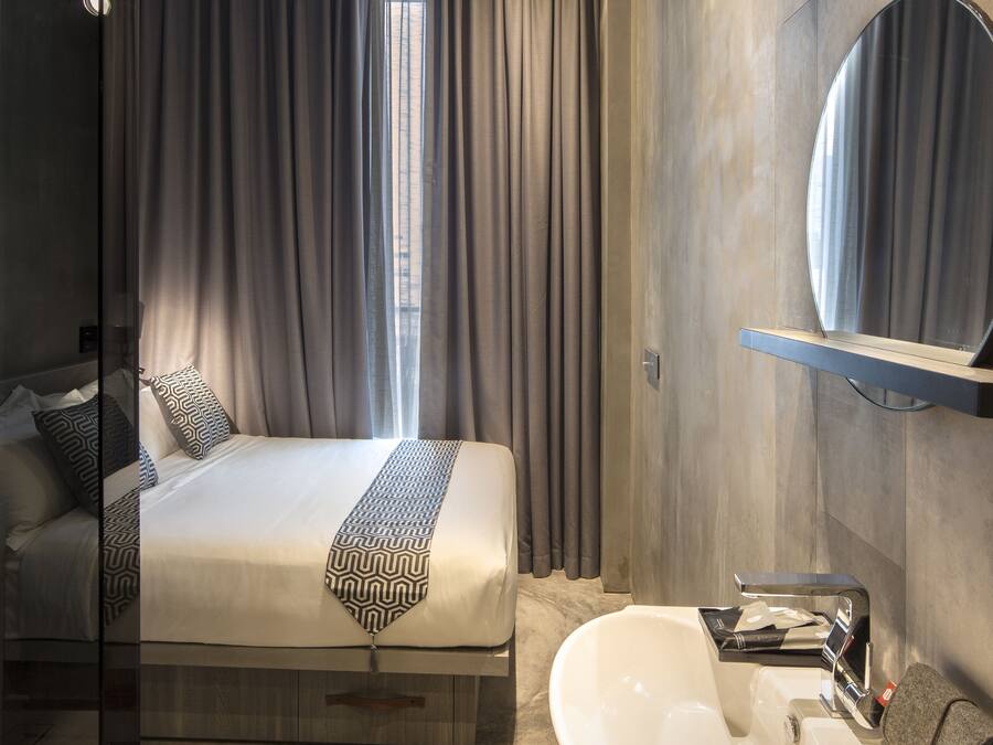 Una habitación de hotel moderna con una cama grande, cabina de ducha de vidrio, lavamanos integrado y un espejo amplio.