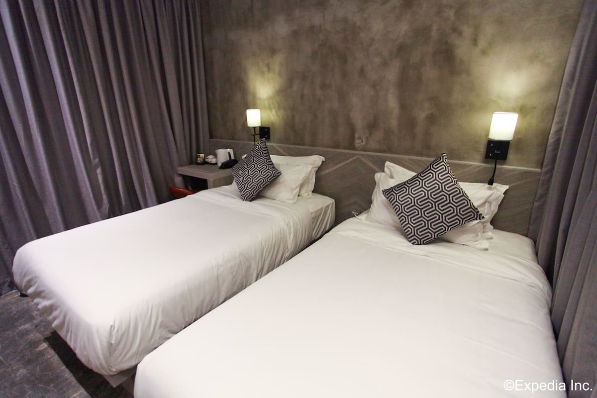 Hotellihuone, jossa on kaksi erillistä sänkyä, ja molemmissa on kuviollinen tyyny sekä yöpöytä, jossa on lamppu.